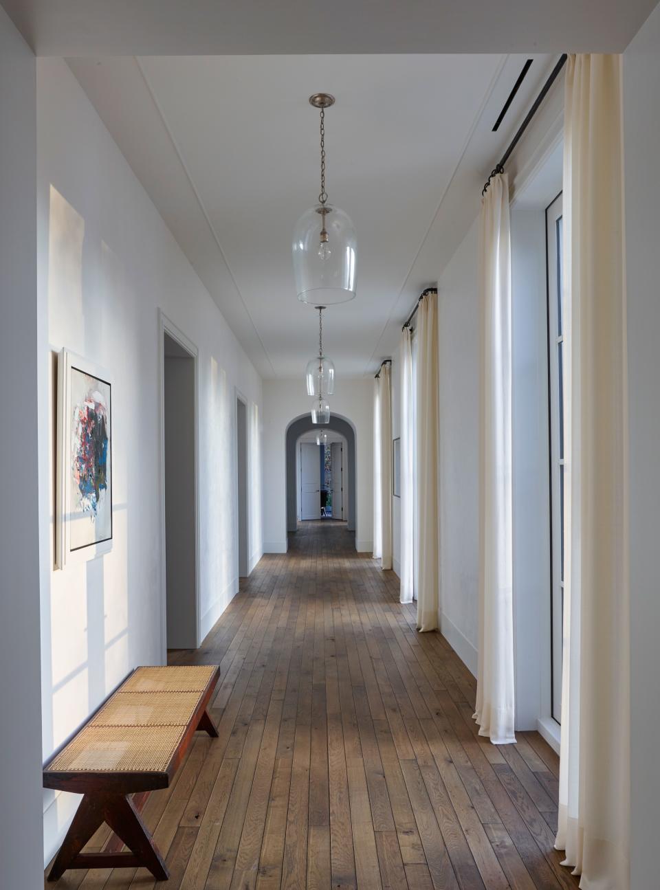 Oak plank flooring recalls those found in French residences and adds warmth against the crisp white walls. Rose Uniacke pendants hang in a hallway where a vintage Pierre Jeanneret bench sits beneath artwork by Cy Twombly.