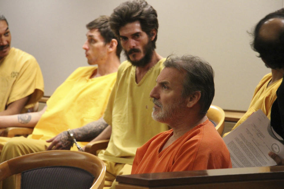 Brian Steven Smith wearing an orange shirt sits with unidentified suspects in a courtroom in Anchorage, Alaska Monday, Oct. 21, 2019. Smith entered an innocent plea Monday in an Anchorage courtroom. He earlier pleaded not guilty in the death of 30-year-old Kathleen Henry, a homeless Alaska Native woman. During his interrogation, police say he confessed to killing another Alaska Native woman. Police won't say if there may be other victims. (AP Photo/Mark Thiessen)