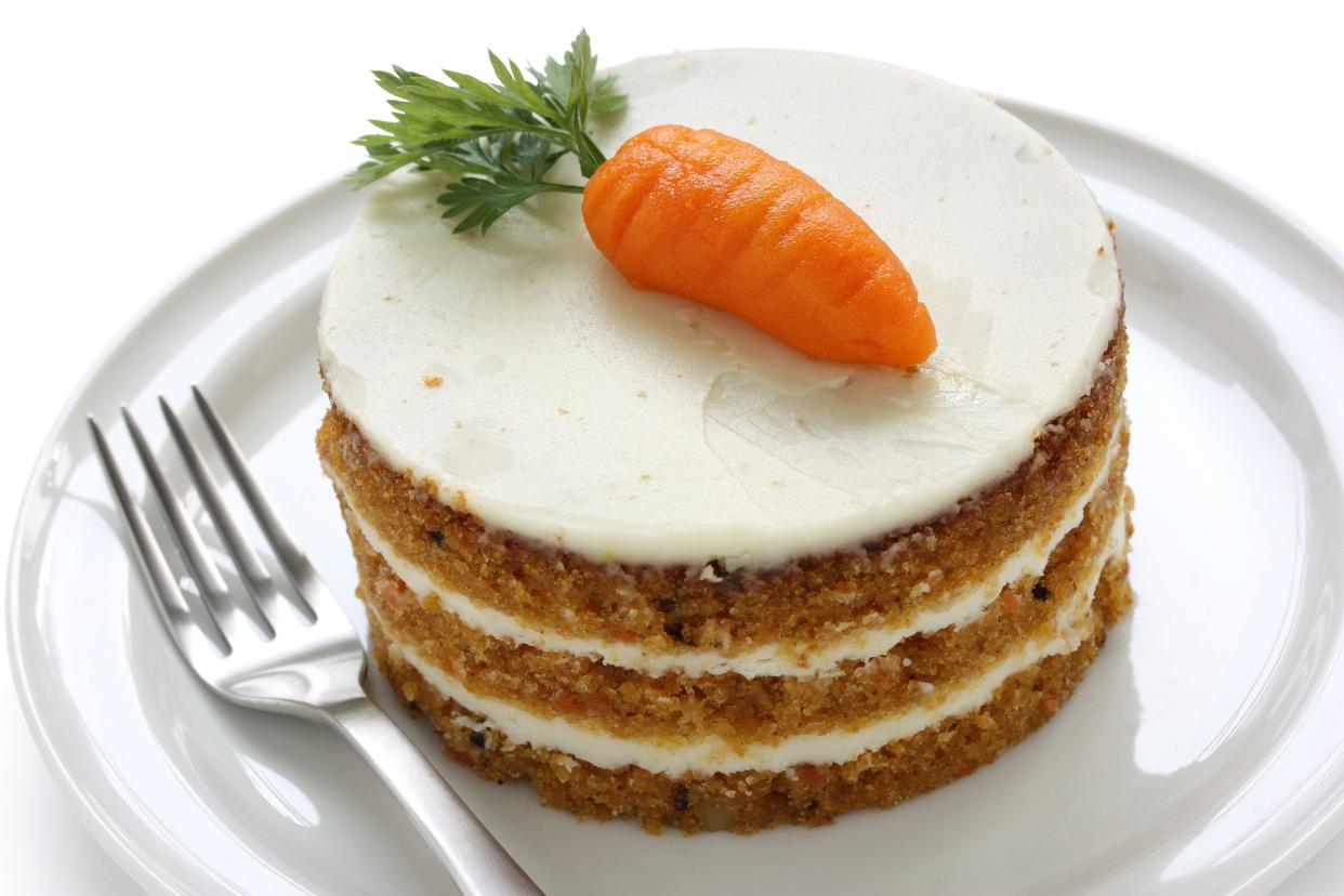 One round diabetic friendly carrot cake tower on a white plate with a fork on a white background