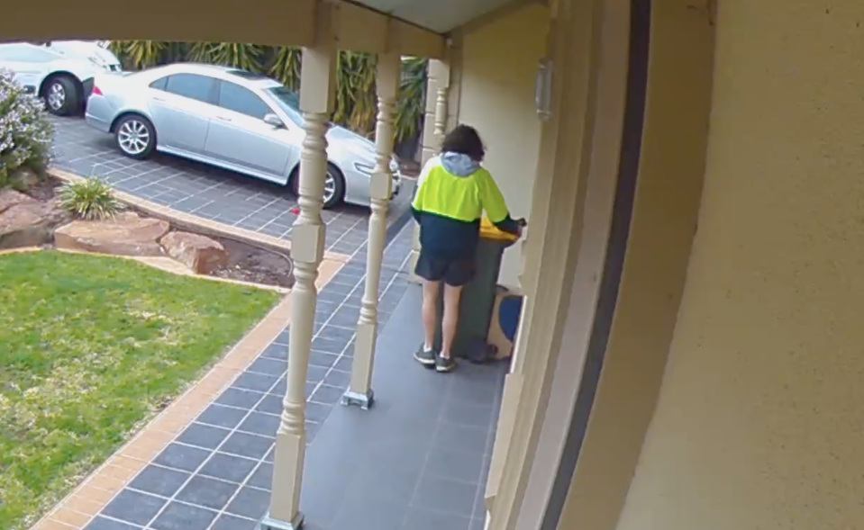 Australia Post worker moves a wheelie bin to hide a parcel at an Adelaide home. 