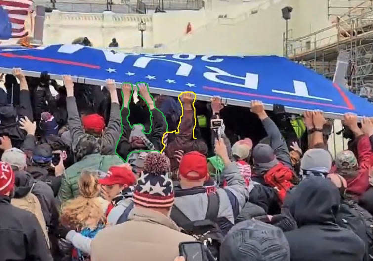 Defendant Marshall Neefe's right hand is visible, in yellow, as he and others pushed a “TRUMP” sign into a line of Metropolitan Police Department officers on Jan. 6, 2021, at the Capitol. (U.S. District Court for D.C.)