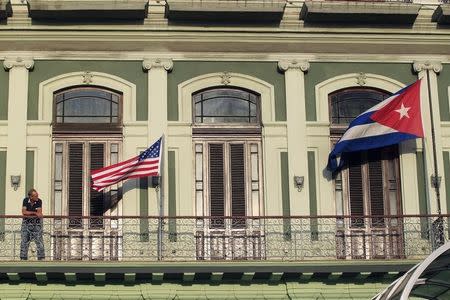 A man stands near the national flags of the U.S. and Cuba (R) on the balcony of a hotel being used by the first U.S. congressional delegation to Cuba since the change of policy announced by U.S. President Barack Obama on December 17, in Havana, January 19, 2015. REUTERS/Stringer