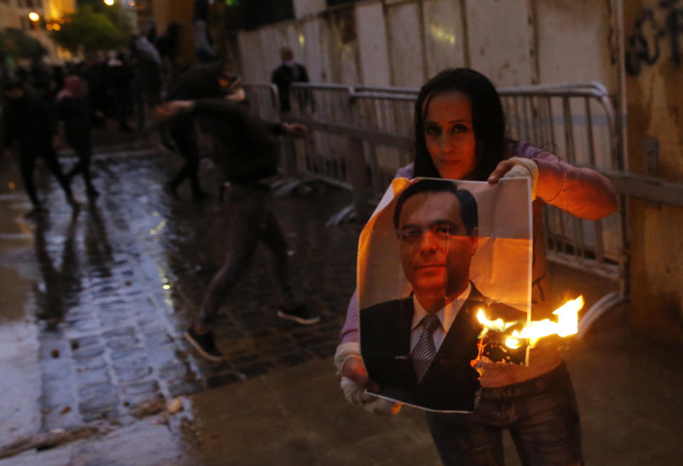 An anti-government protester burns a picture of new Lebanese Prime Minister Hassan Diab during ongoing protests in Beirut, Lebanon, Wednesday, Jan. 22, 2020. Lebanon's new government held its first meeting Wednesday, a day after it was formed following a three-month political vacuum, with the prime minister saying his Cabinet will adopt financial and economic methods different than those of previous governments. (AP Photo/Bilal Hussein)