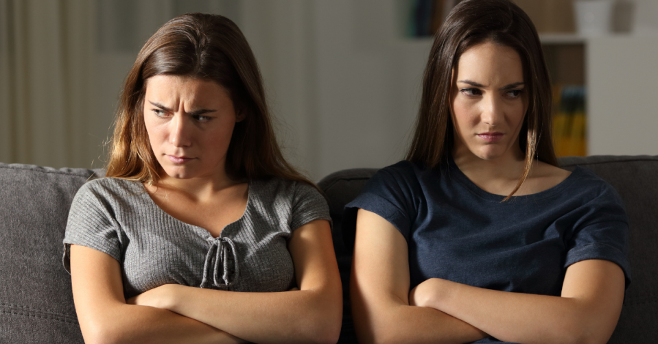 Two women sit angrily on a couch with their arms crossed.