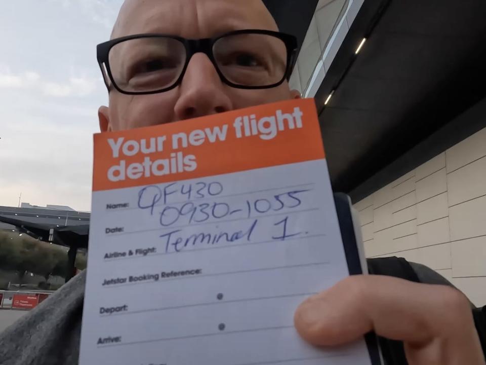 A man holding a sign that shows new flight details.