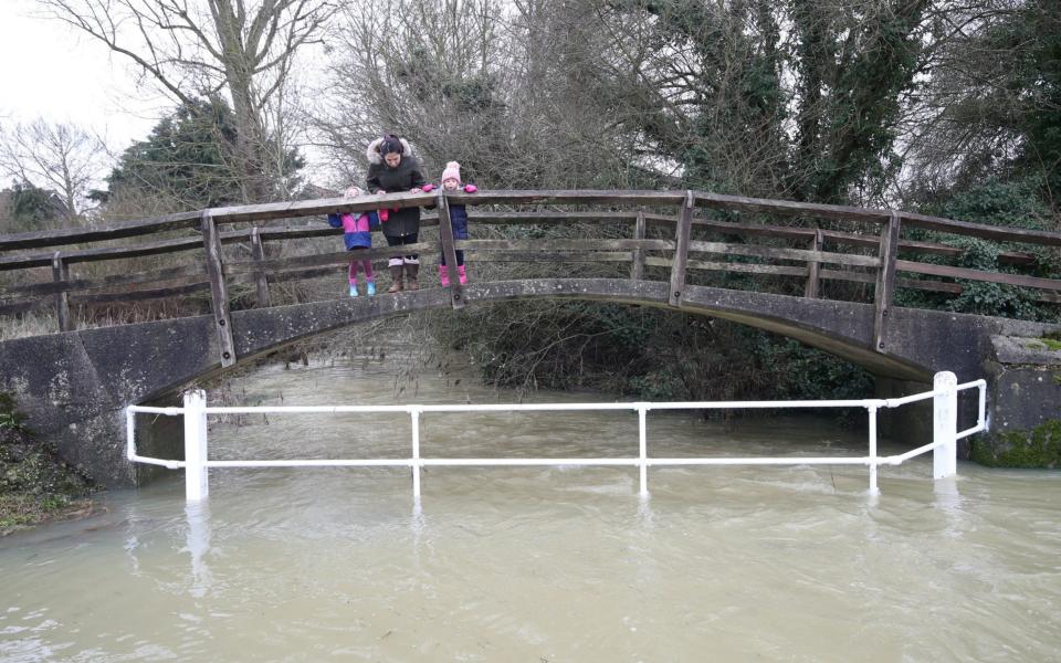 People crossing a bridge over a flooded river in Great Easton, Essex - Yui Mok/PA