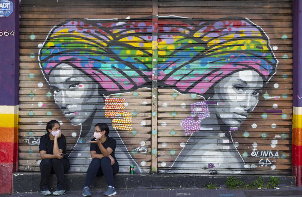 Dos mujeres hablando ante una tienda de moda cerrada por las medidas de confinamiento para contener la expansión del nuevo coronavirus, en Sao Paulo, Brasil, el lnes 1 de junio de 2020. (AP Foto/Andre Penner)