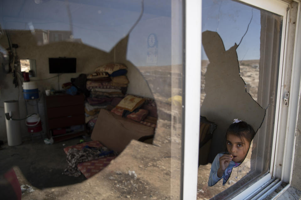 A Palestinian girl is seen through her family house's shattered window following a settlers' attack from nearby settlement outposts on the Bedouin community, in the West Bank village of al-Mufagara, near Hebron, Thursday, Sept. 30, 2021. Israeli settler attack last week damaged much of the village’s fragile infrastructure. (AP Photo/Nasser Nasser)