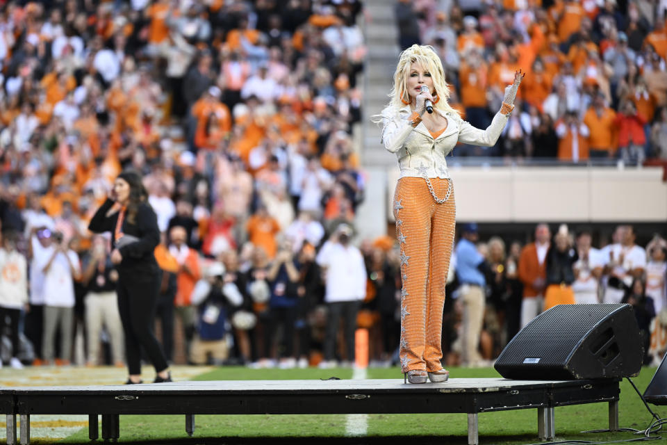 Dolly Parton performs at stadium in a silver blazer and orange pants