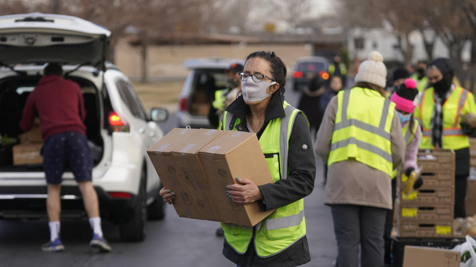 A volunteer carries food to waiting cars at the Utah Food Bank's mobile food pantry Thursday, March 11, 2021, in West Valley City, Utah. Since the coronavirus pandemic began many have relied more on food banks to get enough to eat. (AP Photo/Rick Bowmer)