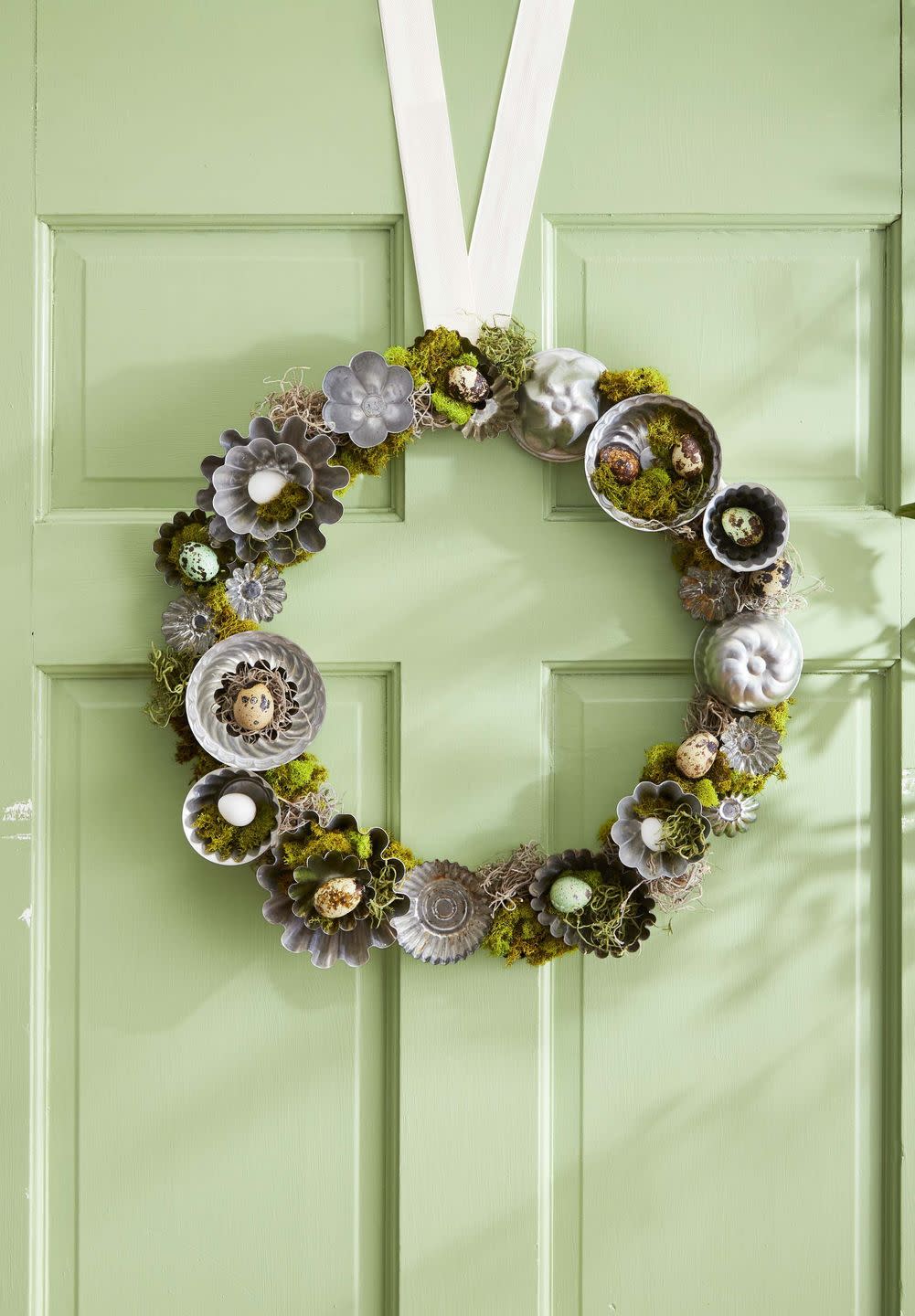 handcrafted moss wreath decorated with faux quail eggs and small tart tins to mimic nests, hung on green door