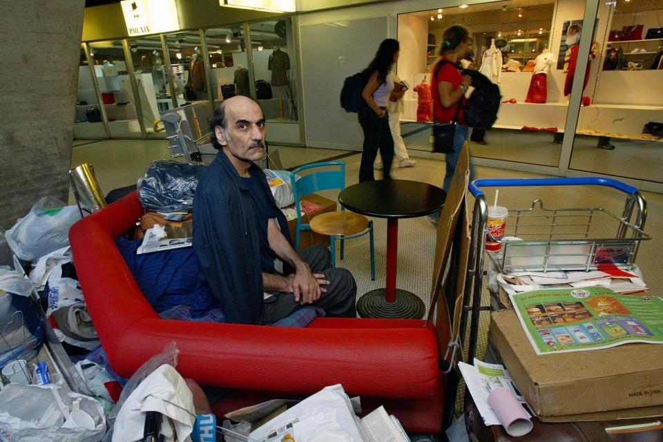 FILE - Merhan Karimi Nasseri sits among his belongings at Terminal 1 of Roissy Charles De Gaulle Airport, north of Paris on Aug. 11, 2004 . An Iranian man who lived for 18 years in Paris' Charles de Gaulle Airport and inspired the Steven Spielberg film "The Terminal" died Saturday, Nov. 12, 2022 in the airport, officials said. Merhan Karimi Nasseri died after a heart attack in the airport's terminal 2F around midday, according an official with the Paris airport authority. Police and then a medical team treated him but were not able to save him, the official said. (AP Photo/Michel Euler, File)