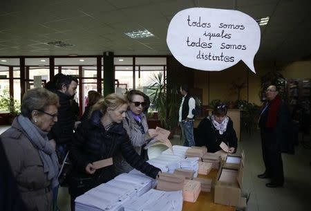 Voters select their ballots at a polling station with a sign hanging over the table which reads "We are all the same, we are all different" during voting in Spain's general election in Madrid, Spain, December 20, 2015. REUTERS/Andrea Comas