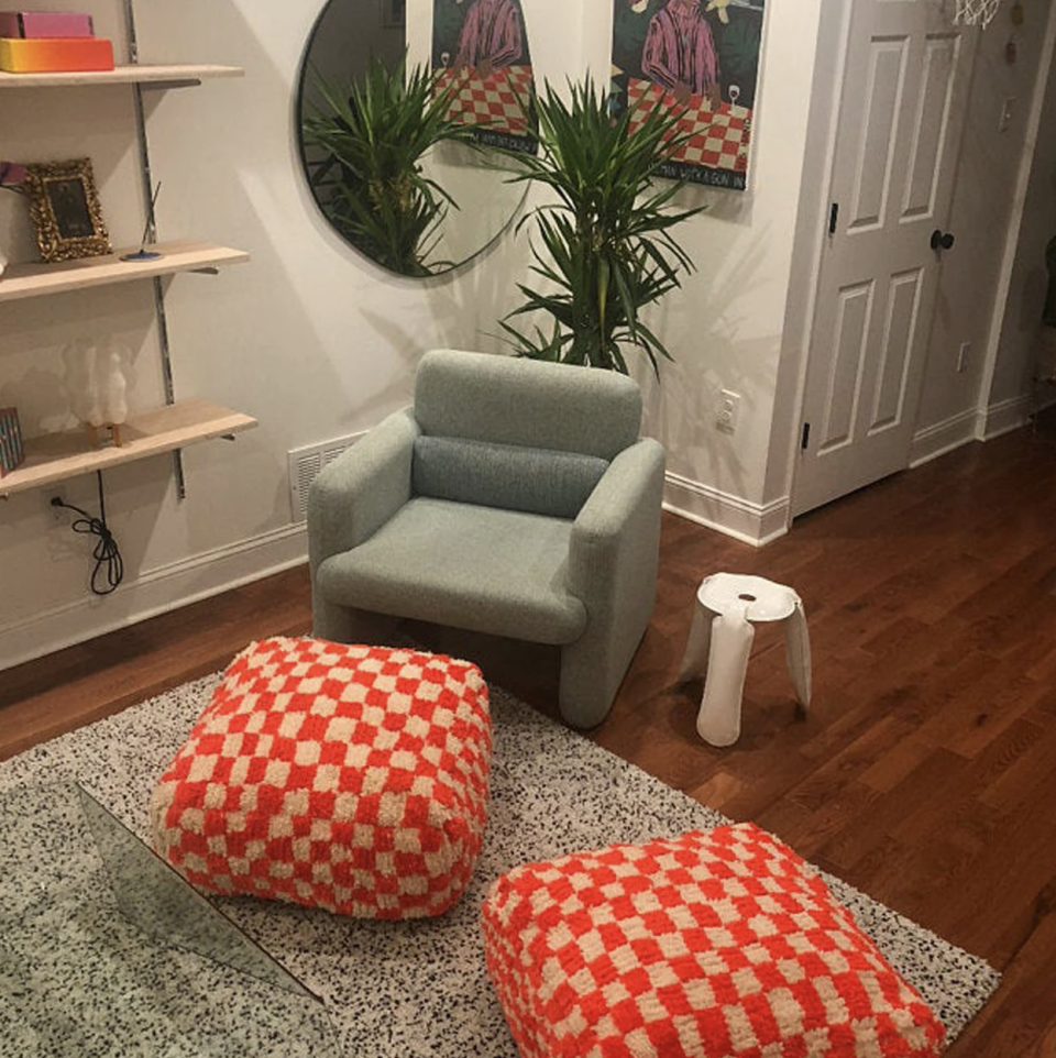 Moroccan Checkered Pouf in red and beige in living roof with rug, chair, plant and mirror (photo via Etsy)