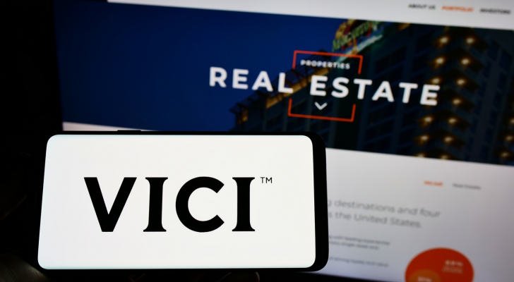 Person holding mobile phone with logo of American real estate company Vici Properties Inc. on screen in front of web page. VICI stock.