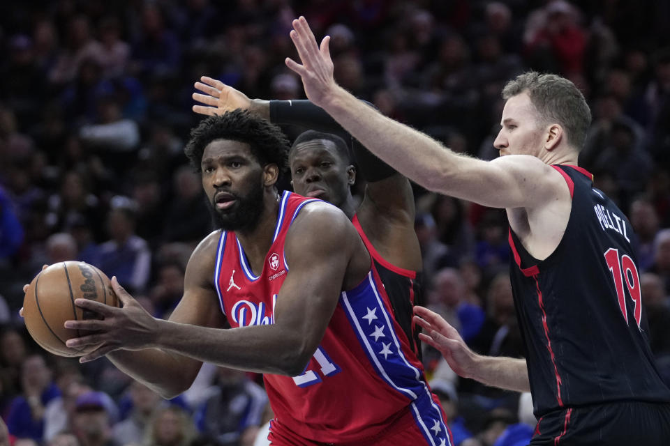 Philadelphia 76ers' Joel Embiid, left, tries to get by Toronto Raptors' Dennis Schroder, center, and Jakob Poeltl during the first half of an NBA basketball game, Friday, Dec. 22, 2023, in Philadelphia. (AP Photo/Matt Slocum)