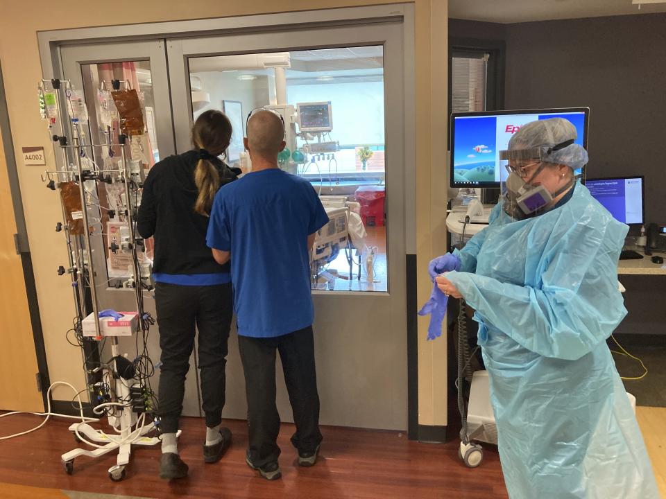 Two visitors peer into the room of a COVID-19 patient in the intensive care unit at Salem Hospital in Salem, Oregon, on Friday, Aug. 20, 2021, as a nurse dons full protective gear before going into the room of another patient. The hospitalization rate of unvaccinated COVID-19 is breaking records and squeezing hospital capacity, with several running out of room to take more patients. (AP Photo/Andrew Selsky)