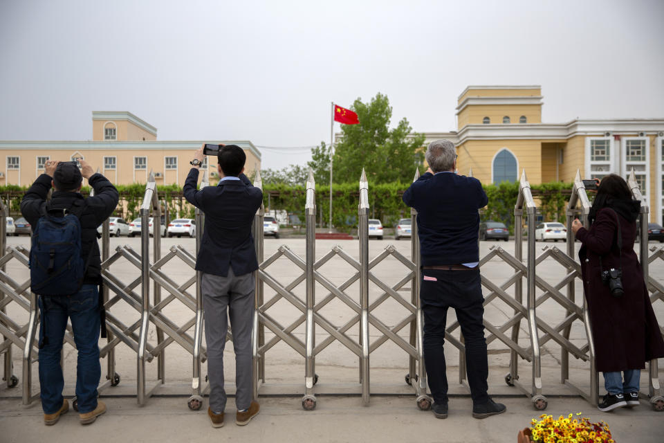 Journalists and government officials take photos outside a location that was identified in early 2020 as a re-education facility by an Australian think tank, which the Chinese government asserts is currently home to a veterans' affairs bureau and other offices, in Turpan in western China's Xinjiang Uyghur Autonomous Region during a government organized trip for foreign journalists, Thursday, April 22, 2021. A spokesperson for the Xinjiang region called accusations of genocide "totally groundless" as the British parliament approved a motion Thursday that said China's policies amounted to genocide and crimes against humanity. (AP Photo/Mark Schiefelbein)