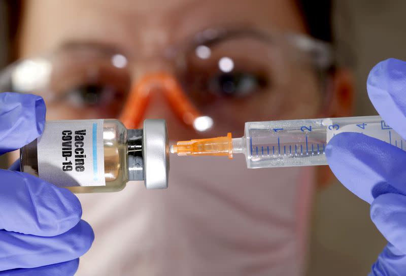 FILE PHOTO: A woman holds a small bottle labeled with a "Vaccine COVID-19" sticker and a medical syringe in this illustration