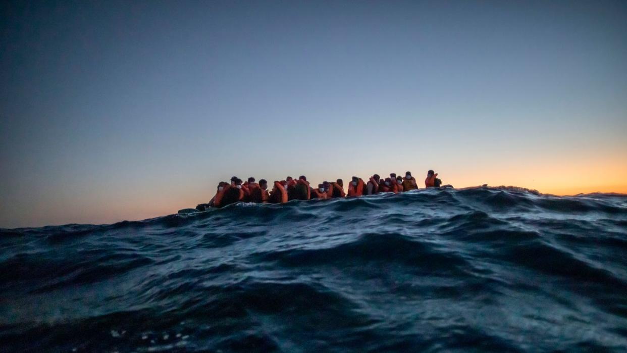 Migranten aus verschiedenen afrikanischen Nationen warten in einem Boot vor der libyschen Küste im Mittelmeer auf Helfer.