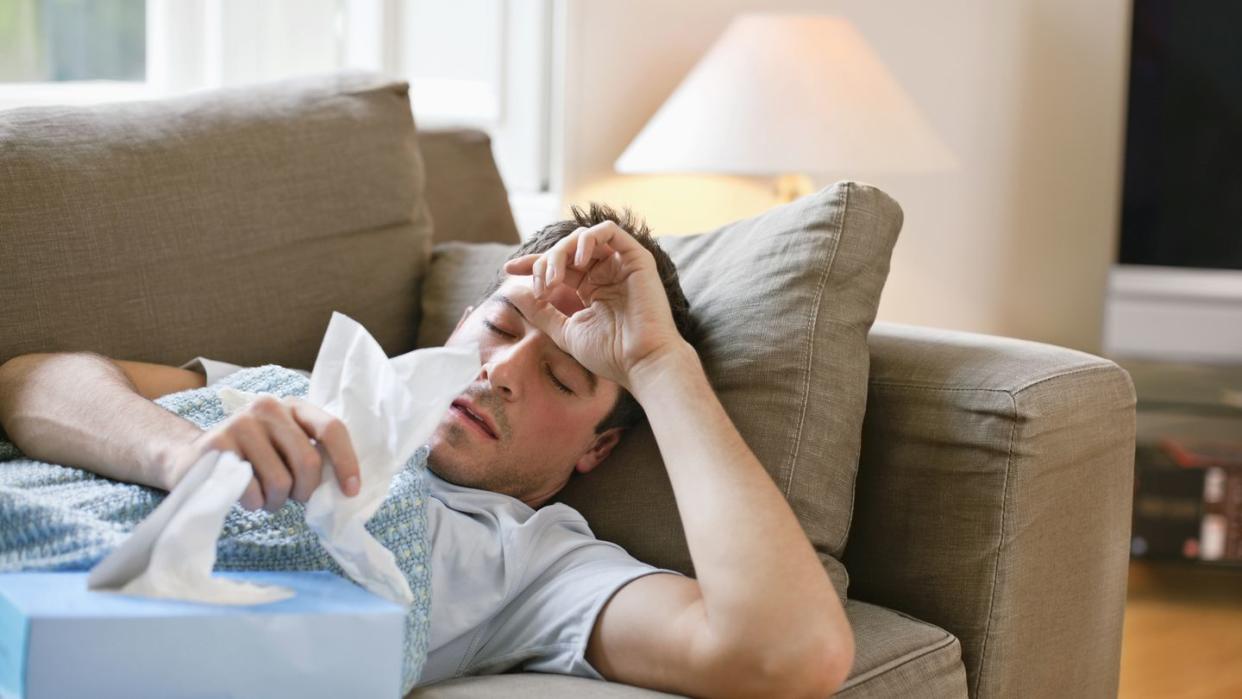 man with a cold lying in sofa holding tissues