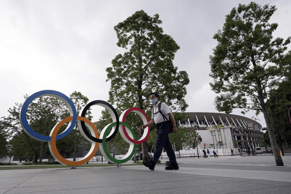 A man wearing a mask against the spread of the new coronavirus walks at the Olympic rings in front of the New National Stadium Wednesday, July 22, 2020, in Tokyo. The postponed Tokyo Olympics have again reached the one-year-to-go mark. But the celebration is small this time with more questions than answers about how the Olympics can happen in the middle of a pandemic. That was before COVID-19 postponed the Olympics and pushed back the opening to July 23, 2021. (AP Photo/Eugene Hoshiko)