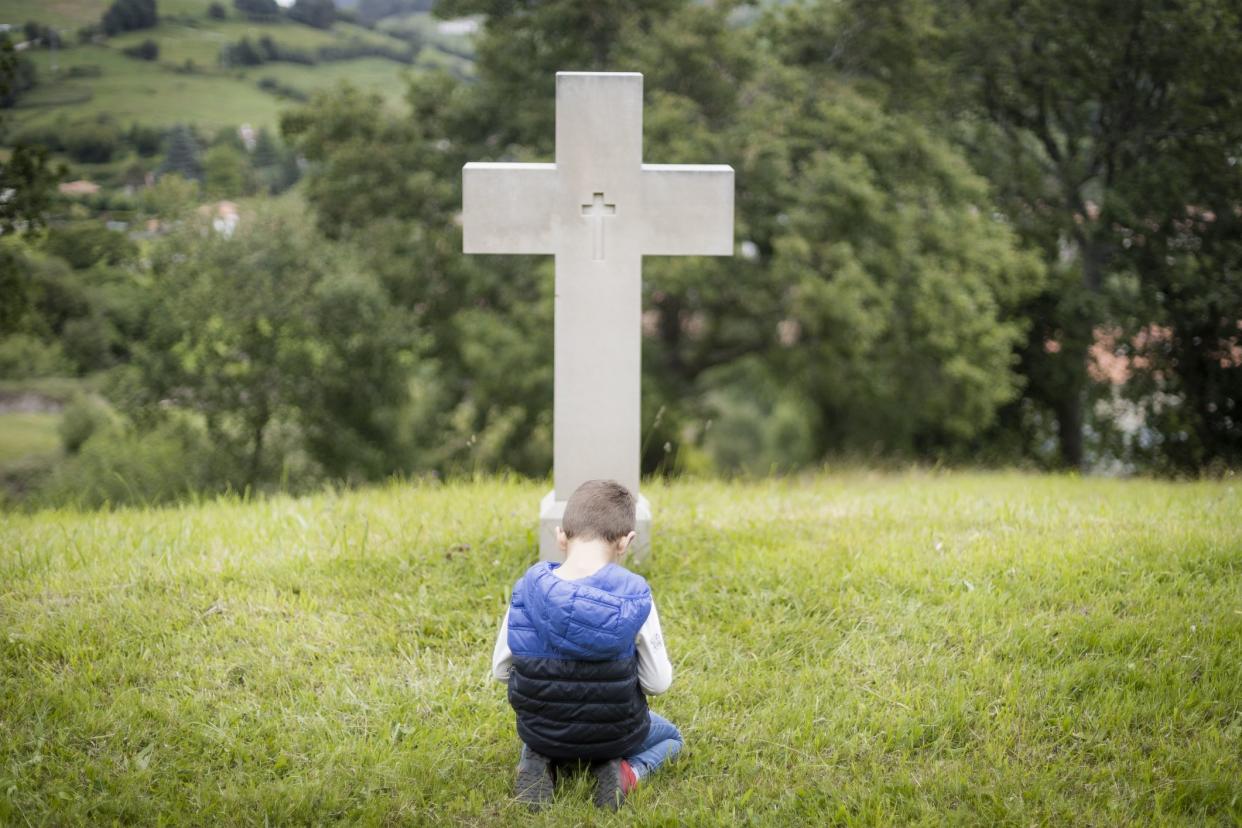 Little boy praying in front of a cross