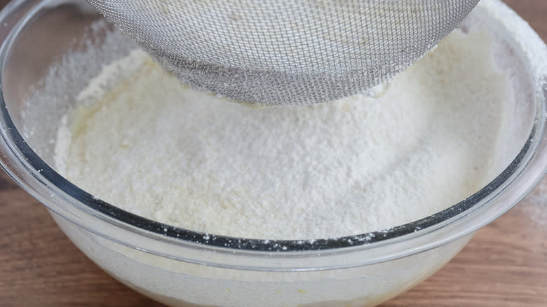 flour being sifted into clear bowl