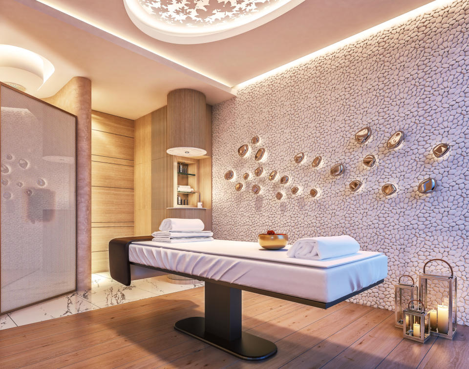 A spa room with a modern massage table with folded towels, mood lighting, a stone accent wall with decorative shells and a lantern cluster on the floor