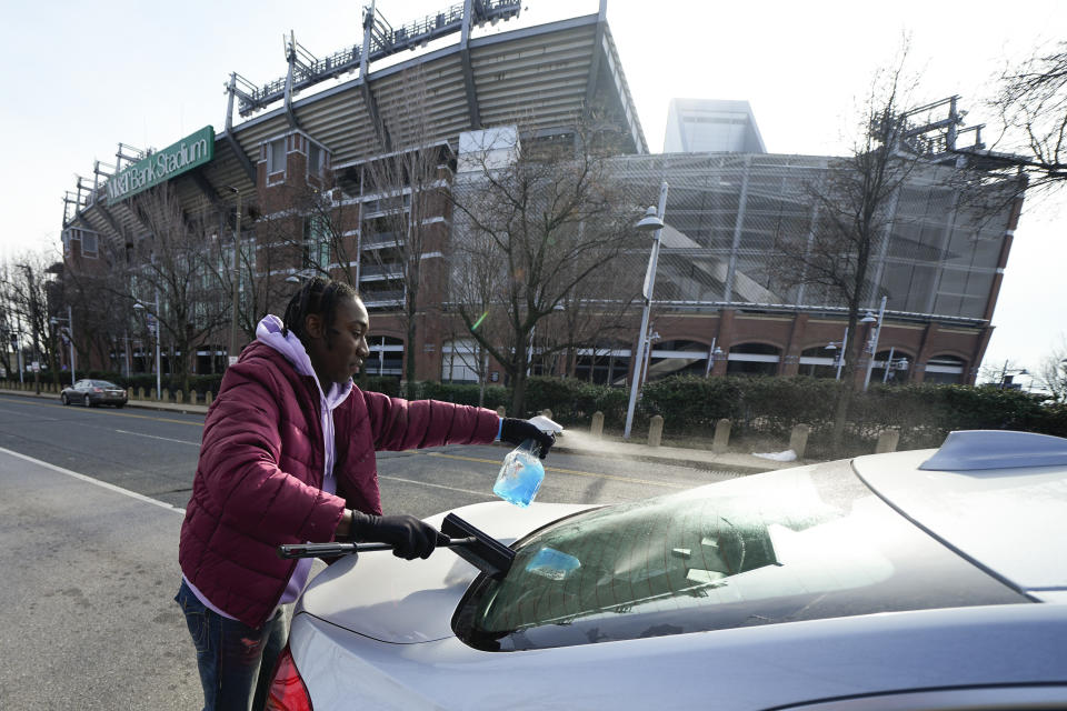 Shamonte Jones cleans the back windshield of a vehicle stopped at a red light near M&T Bank Stadium, Tuesday, Jan. 10, 2023, in Baltimore. Local officials are rolling out their latest plan to steer squeegee workers away from busy downtown intersections and toward formal employment using law enforcement action and outreach efforts. (AP Photo/Julio Cortez)
