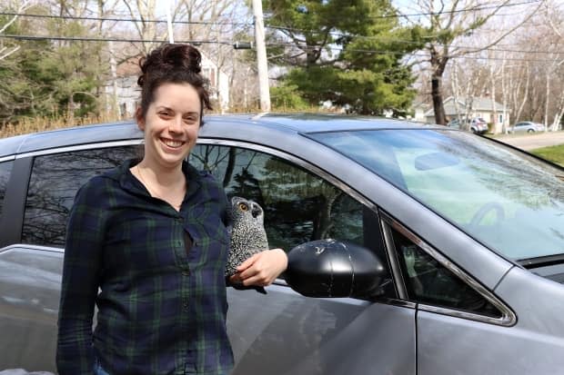 Cassie Gilmour holds a decoy owl next to her minivan that has been under attack from a robin.  (Brittany Wentzell/CBC - image credit)