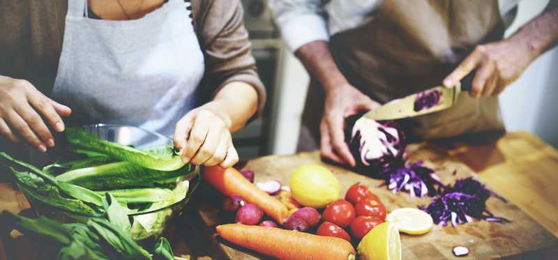 Two people in aprons prepping fresh ingredients to cook.