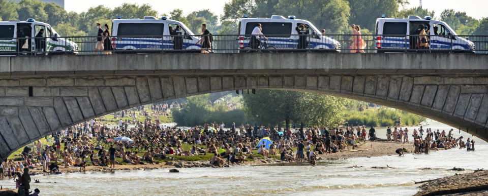 Police cars stand on a bridge next to hundreds of people staying at the banks of the river Isar after ongoing relaxing of measures against the coronavirus outbreak in Munich, Germany, Saturday, June 13, 2020. (Peter Kneffel/dpa via AP)