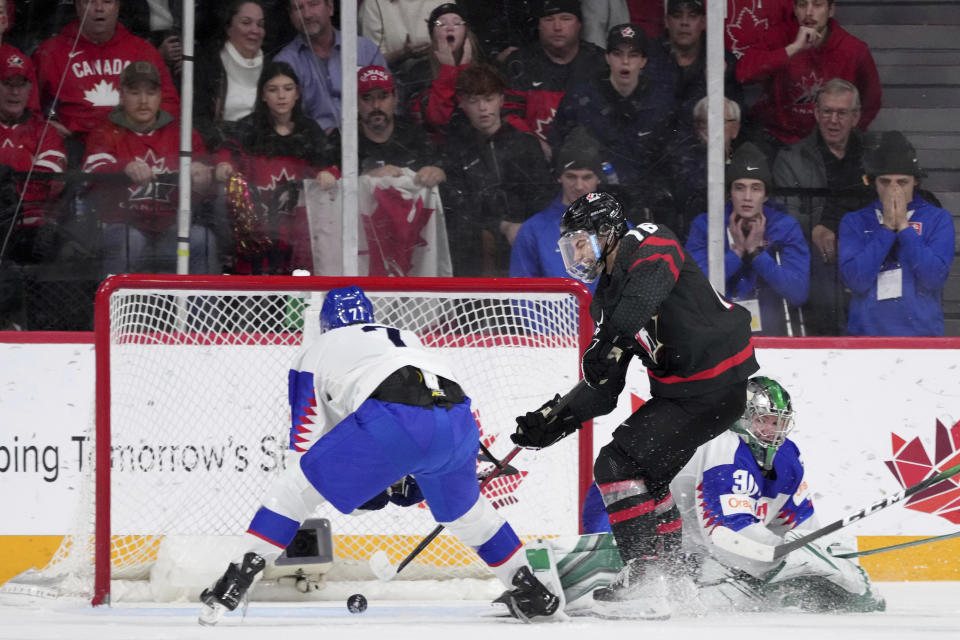 Canada's Connor Bedard, center, scores the winning goal past Slovakia goaltender Jan Korec, right, and Simon Nemec during overtime of IIHF world junior hockey championship quarterfinals action in Halifax, Nova Scotia, Monday, Jan. 2, 2023. (Darren Calabrese/The Canadian Press via AP)