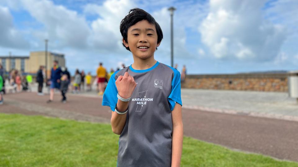 Sebastian smiles at the camera holding his silver wristband as you can see other children racing the junior Parkrun in the background