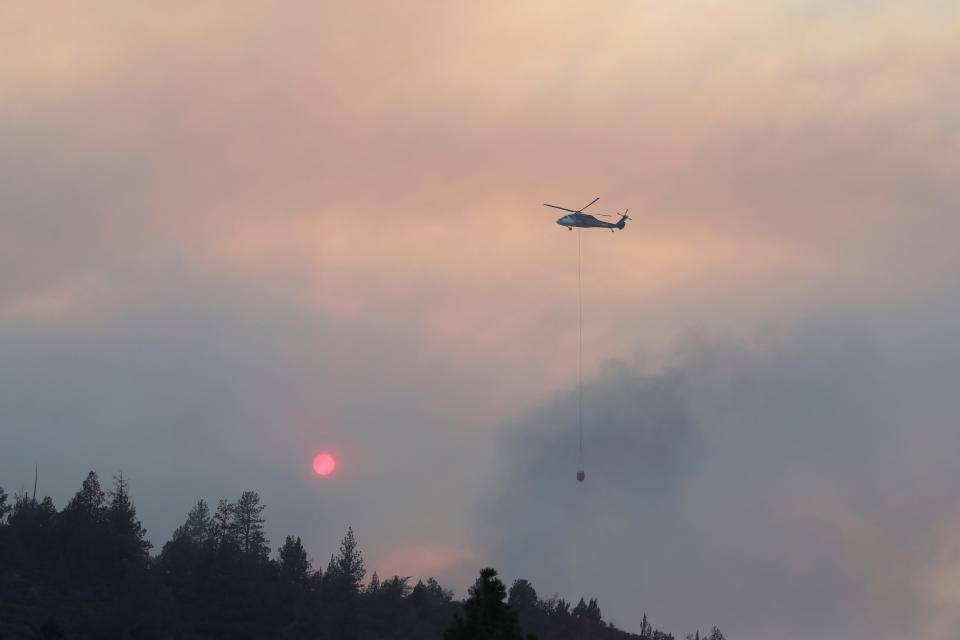 A helicopter carries water over a ridge to douse flames from a wildfire called the Mill Fire in the Lake Shastina Subdivision, northwest of Weed, Calif., Friday, Sept. 2, 2022.