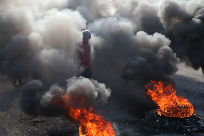 An Iraqi demonstrator walks next to burning tires blocking a road, during ongoing anti-government protests, in Kerbala