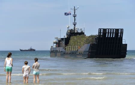 People walk in the sea as British landing craft are seen behind on the 70th anniversary of the D-Day landings at Gold Beach at Arromanches-les-Bains on the Normandy coast, June 6, 2014. REUTERS/Toby Melville