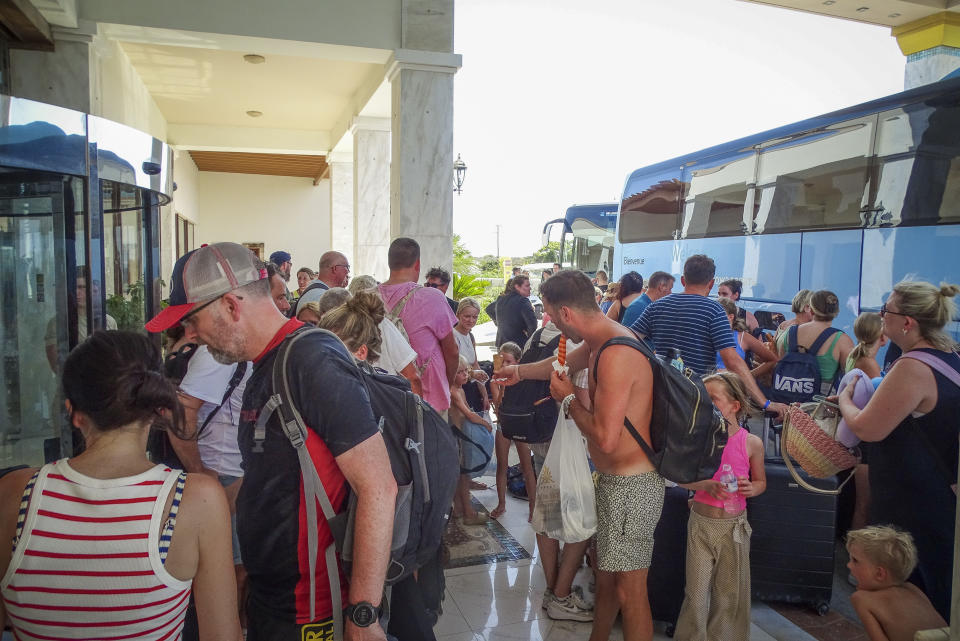 Evacuees wait to board on buses as they leave their hotel during a forest fire on the island of Rhodes, Greece, Sunday, July 23, 2023. Some 19,000 people have been evacuated from the Greek island of Rhodes as wildfires continued burning for a sixth day on three fronts, Greek authorities said on Sunday. (Argyris Mantikos/Eurokinissi via AP)