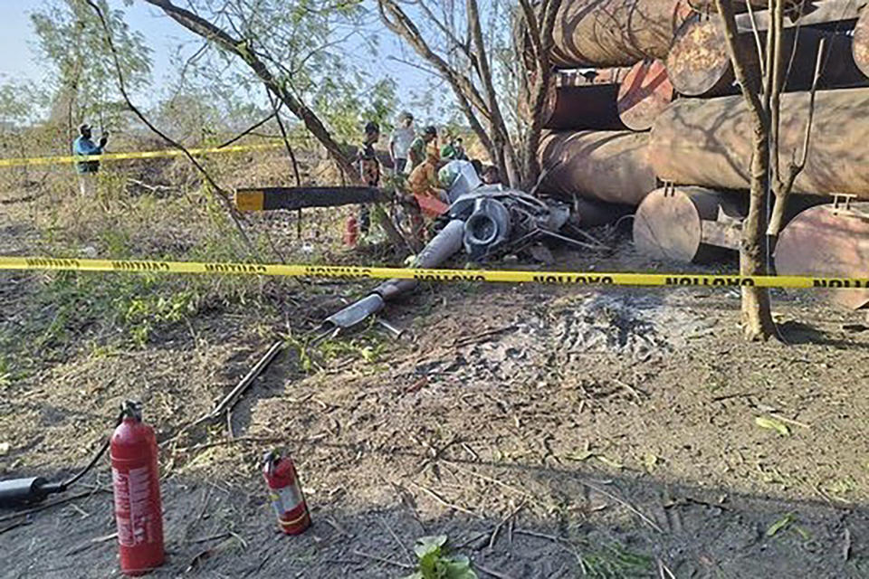 In this photo provided by the Cavite Police Regional Office 4A, rescuers check the remains of a trainer helicopter after it crashed in Cavite province, Philippines on Thursday April 11, 2024. The Philippine navy training helicopter crashed Thursday in a grassy area near a city public market south of the capital, the military and police said. (Cavite Police Regional Office 4A via AP)