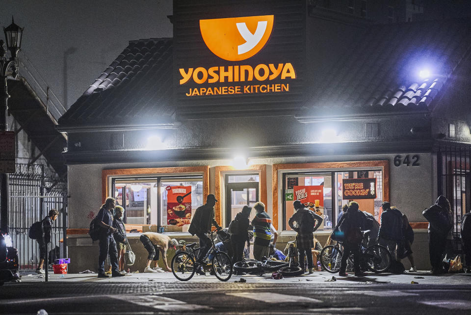 People linger outside a Yoshinoya restaurant across McArthur Park early morning Wednesday, June 26, 2024. The number of homeless residents counted in Los Angeles County has dipped slightly, decreasing by about 0.3% since last year as California continues to struggle with the long-running crisis of tens of thousands of people sleeping in cars and encampments. (AP Photo/Damian Dovarganes)