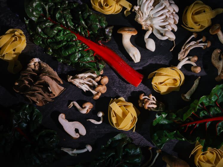 LOS ANGELES, CA - JANUARY 20, 2023: Mushrooms, chard, and pasta sit on a textured tabletop on January 20, 2023 at the Los Angeles Times test kitchen. These ingredients are part of a wild mushroom pasta recipe.