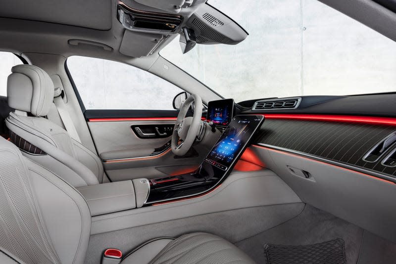 the interior of the 2023 mercedes-amg s 63 e performance sedan, as seen from the passenger seat. the upholstery is dove gray, and orange accent lighting emanates from the dashboard and driver's door