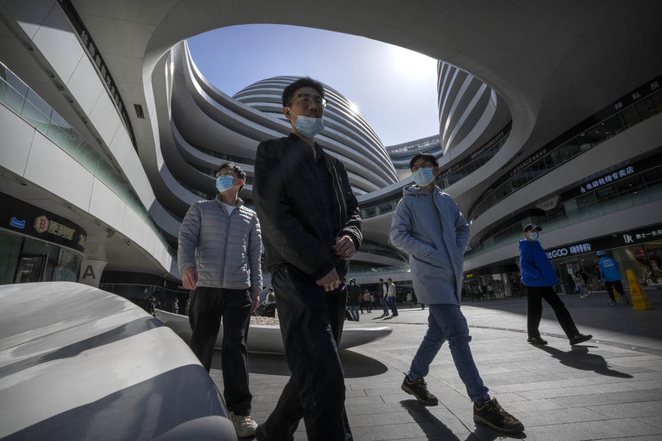 People wearing face masks walk through a shopping and office complex in Beijing, Wednesday, March 1, 2023. (AP Photo/Mark Schiefelbein)