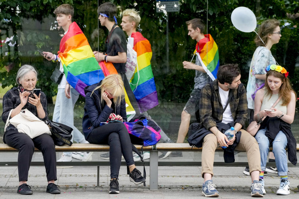 People sit on a bench as participants in Poland's yearly Pride parade, known as the Equality Parade, walk by in Warsaw, Poland, on Saturday June 17, 2023. This year's event was dedicated to transgender rights, which are facing a backlash in many countries. (AP Photo/Czarek Sokolowski)