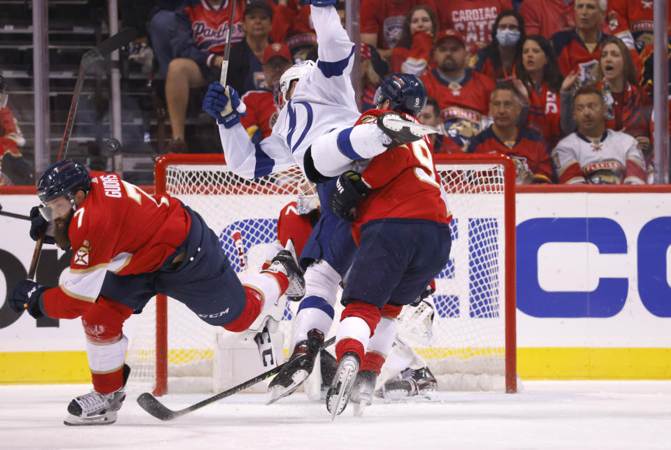 Florida Panthers center Sam Bennett (9) upends Tampa Bay Lightning left wing Nicholas Paul, top, as Florida Panthers defenseman Radko Gudas (7) chases down the puck during the second period of Game 1 of an NHL hockey second-round playoff series Tuesday, May 17, 2022, in Sunrise, Fla. (AP Photo/Reinhold Matay)