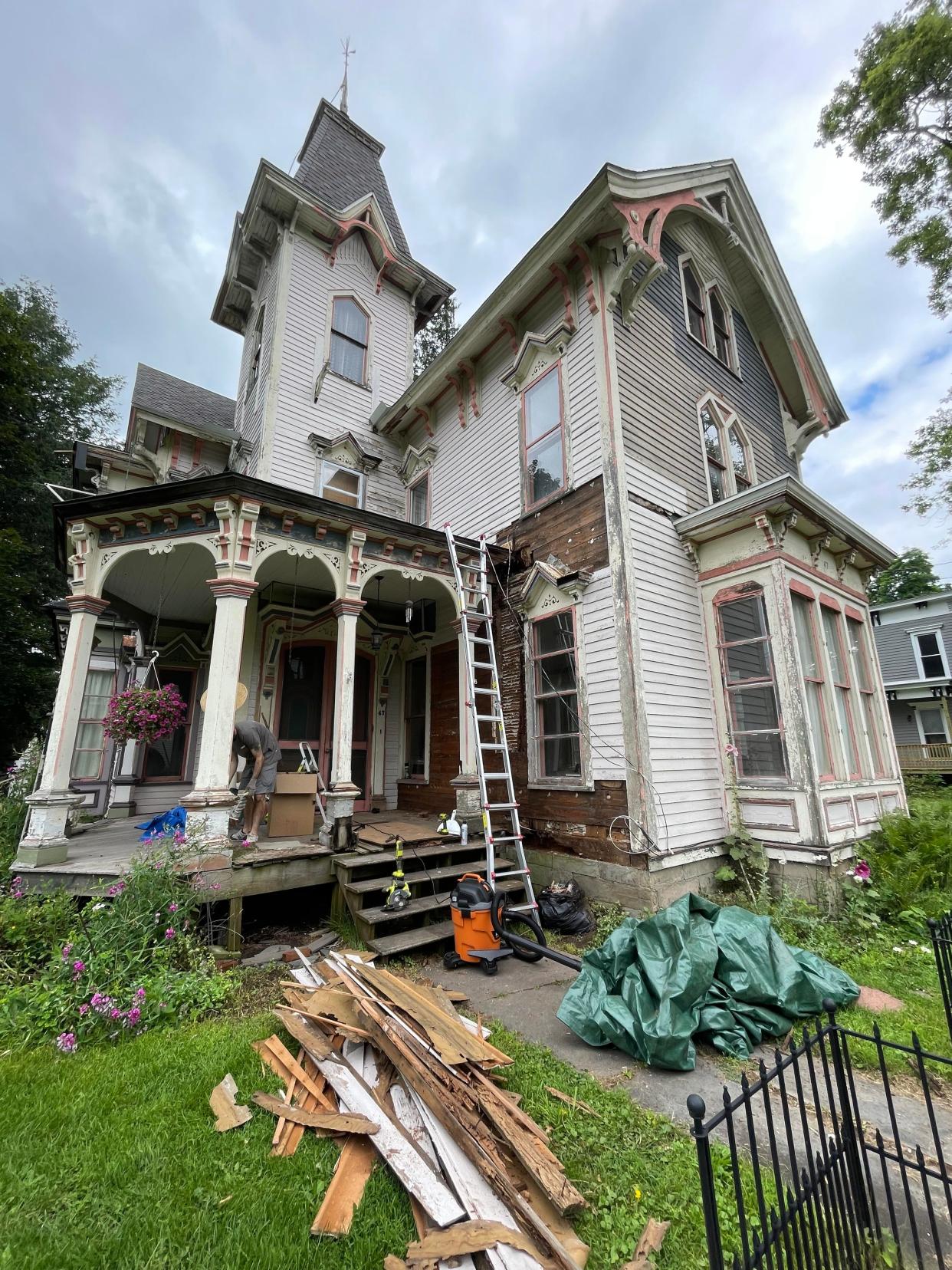 A house with lumber in the front yard and a ladder leaning against it.