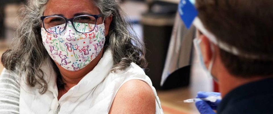 San Diego, CA USA - Mar 17 2021: Woman wearing a mask gets vaccinated in her left arm for covid 19 at a gymnasium in San Diego by a firefighter wearing a face shield
