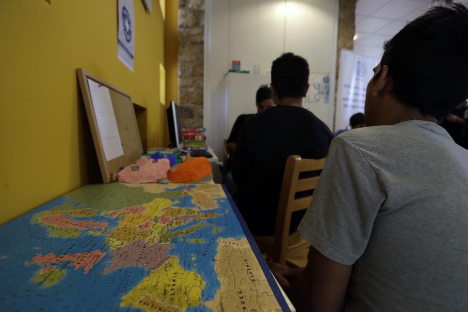 FILE - In this Tuesday, Oct. 11, 2016 file photo migrant children sit near a puzzle, depicting the map of Europe, at a new reception center for unaccompanied minors in Athens. An international human rights organization says on Wednesday, Dec. 18, 2019, that hundreds of unaccompanied children in a migrant camp on the eastern Aegean island of Lesbos are living in "inhuman and degrading" conditions that threaten their mental and physical wellbeing. (AP Photo/Thanassis Stavrakis)