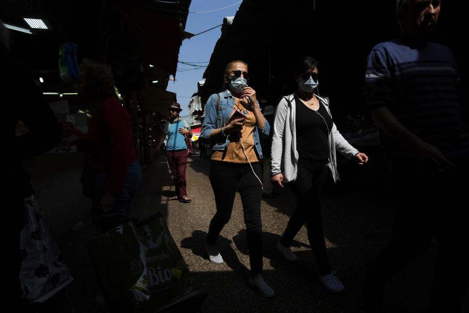 People wear face masks as they shop at a food market in Tel Aviv, Israel, Sunday, March 15, 2020. ‏Israel has imposed a number of tough restrictions to slow the spread of the new coronavirus. Prime Minister Benjamin Netanyahu announced that schools, universities, restaurants and places of entertainment will be closed to stop the spread of the coronavirus. He also encouraged people not to go to their workplaces unless absolutely necessary. (AP Photo/Oded Balilty)